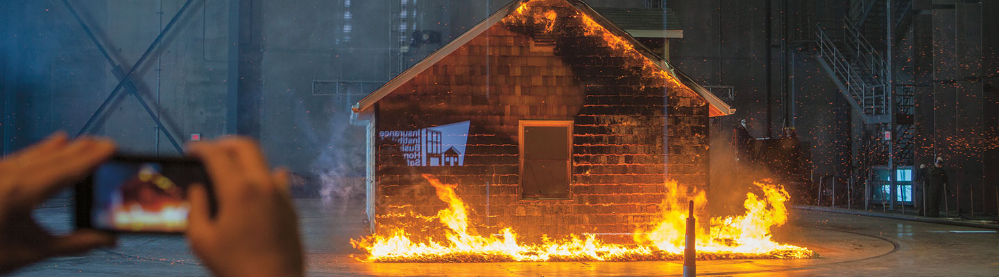 A house burns as someone uses a camera to record it.